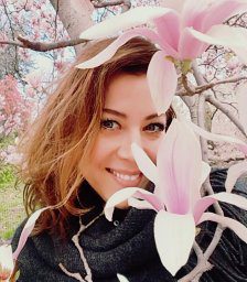 Here's an alt tag suggestion: Woman smiling, partially hidden by magnolia blossoms.